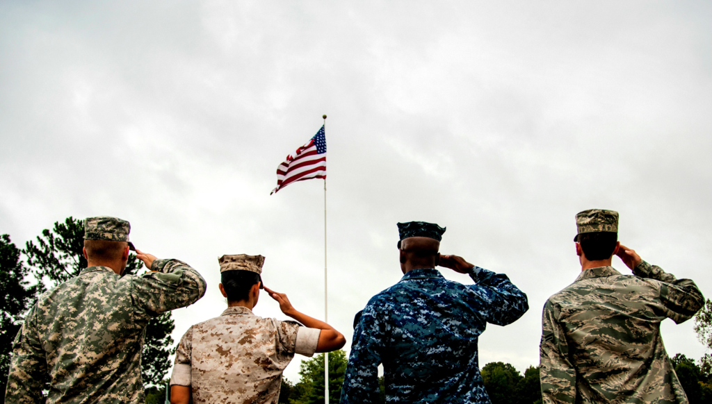 Representatives from each branch of US armed forces soluting American flag