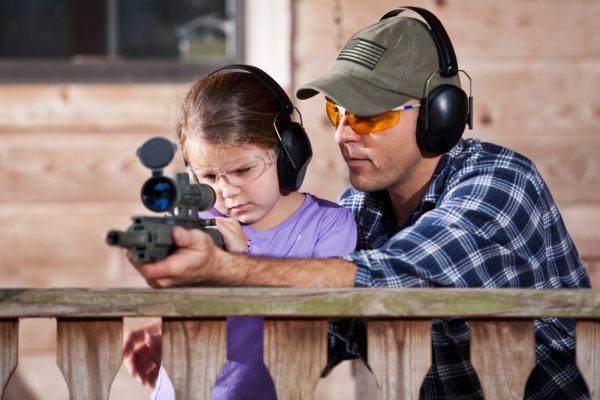 Adult teaching child to shoot rifle