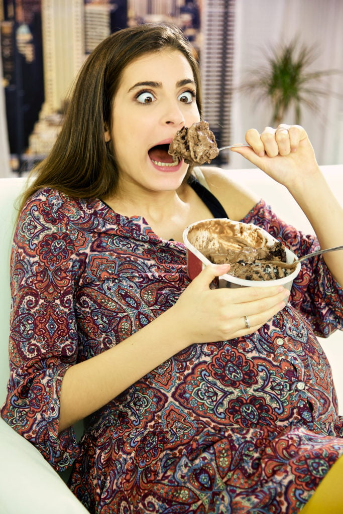 pregnant funny young woman can't resist to devoure a big spoon of ice cream. She has crazy eyes.